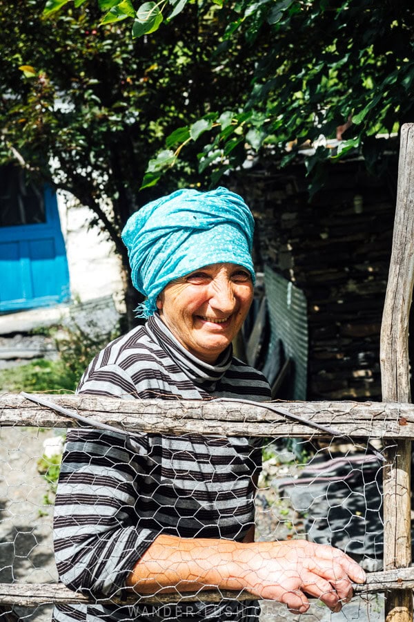 A woman in a blue bandana poses for a photo at her garden gate in the village of Khonischala, Khevsureti.