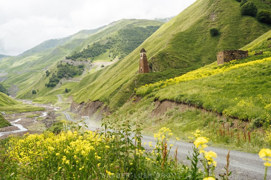 Lebaiskari Tower, an ancient watchtower in a valley in Khevsureti surrounded by green hills with yellow wildflowers.