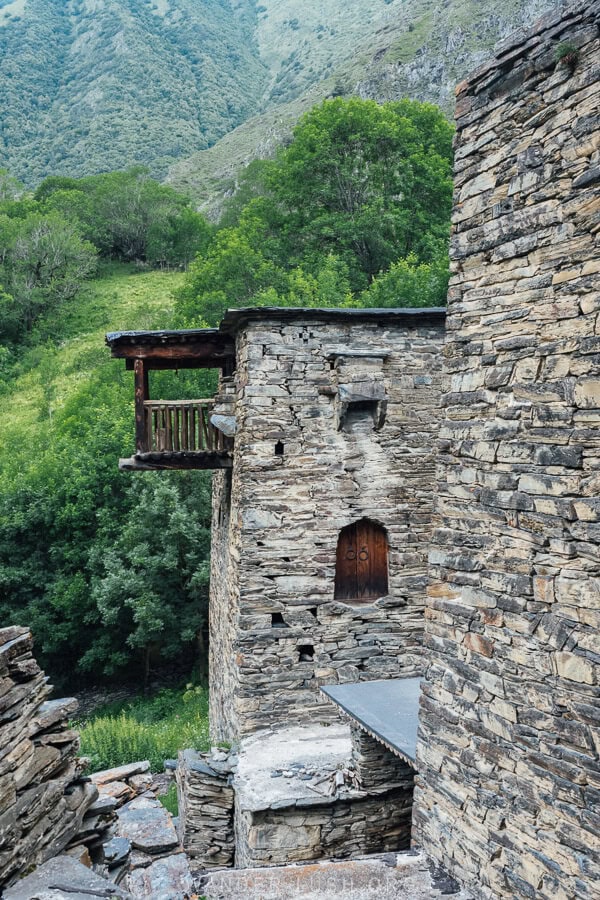 A stone tower in Shatili with a wooden balcony protruding from its top level out towards the green valley.