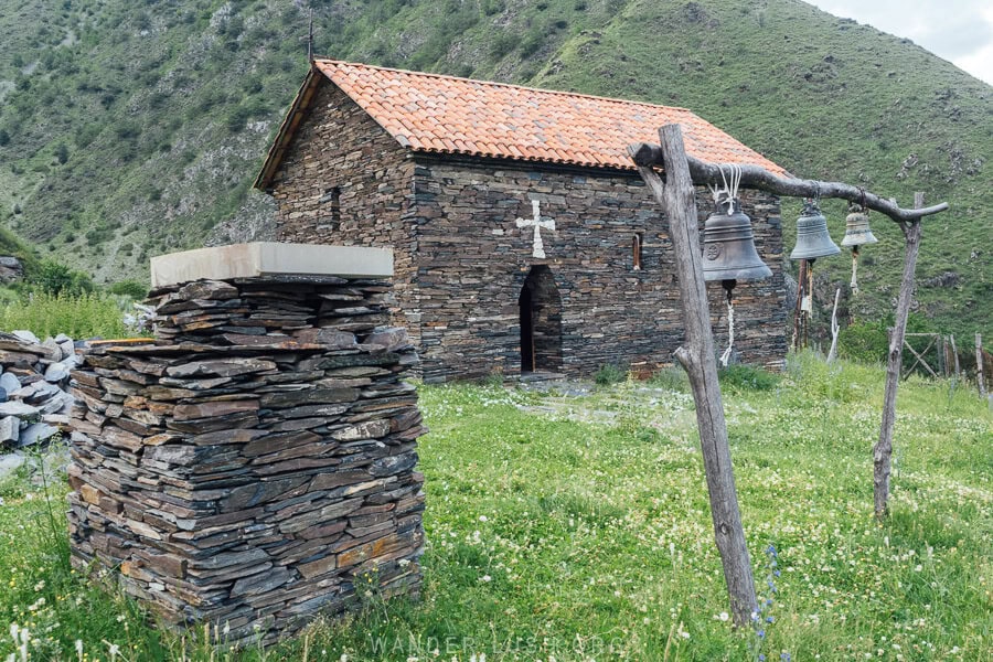 An Orthodox church crafted from stone with a shrine and bells in the yard in Shatili, Georgia.