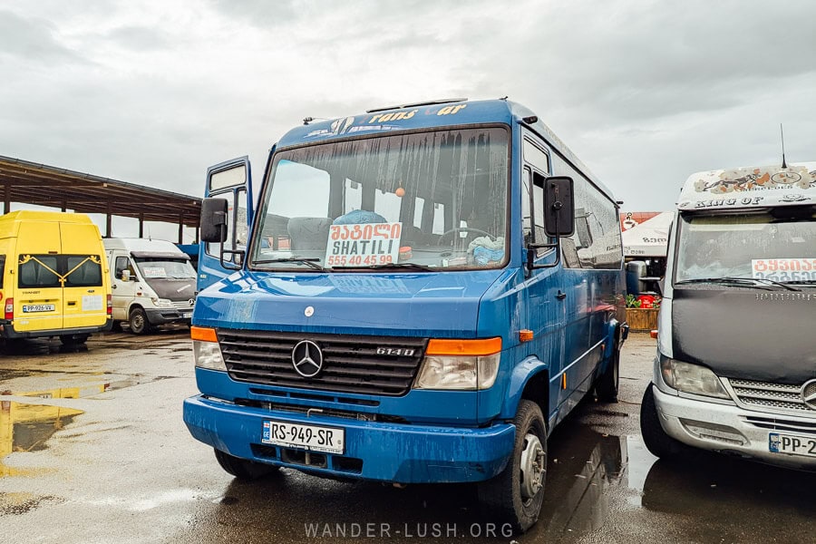 A marshrutka van parked at Didube Bus Station in Tbilisi with a sign on the dashboard reading Shatili.