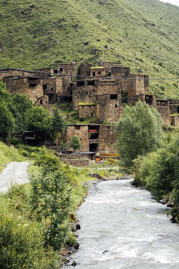 Shatili towers viewed from the riverside, with greenery all around in summer.