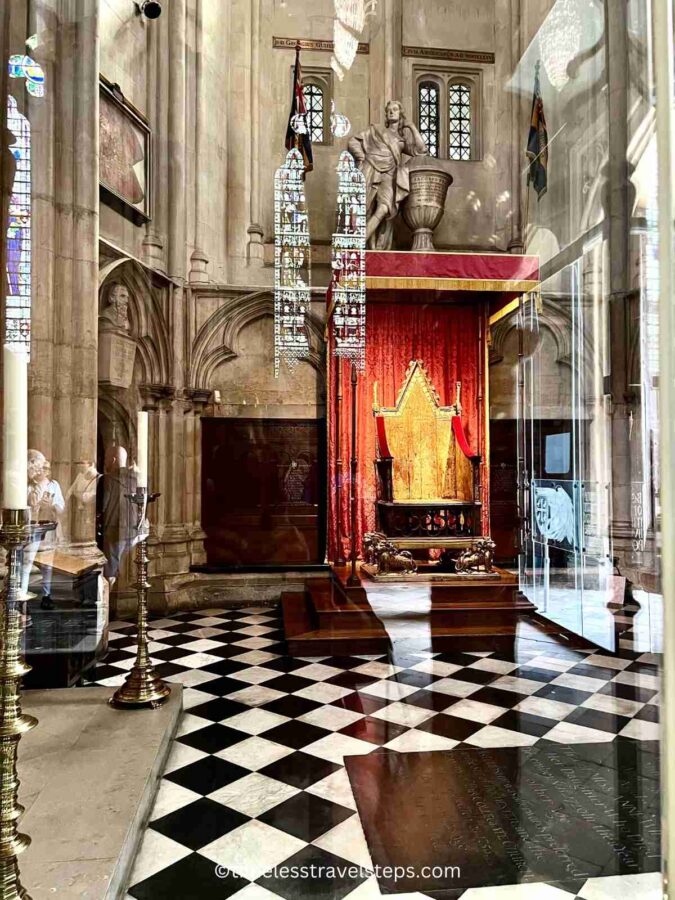 Image of the Coronation Chair near the North Door at Westminster Abbey, enclosed in protective glass. This historic chair is used for the coronation of British monarchs.
