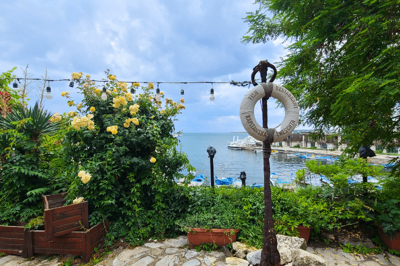 A life preserver hangs aesthetically from a victorian style pole in a leafy garden in front of the sea in Nessebar Bulgaria.