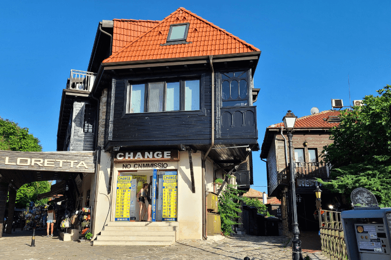 An ancient wooden house painted in black with new orange tile roof stands proudly near the main square in Nessebar Bulgaria. The lower part of the building is white stone and houses a money changer.