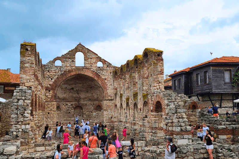 A front view of the peaked back wall of the ruined church of St Sophia in the center of old town Nessebar Bulgaria. The front is open to a sea of tourists, but the side walls made of tall arches are still mostly standing.