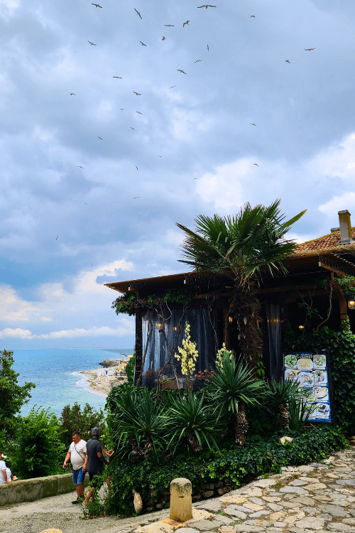 A restaurant overlooks the sea with a picturesque stony path running up the side of it.