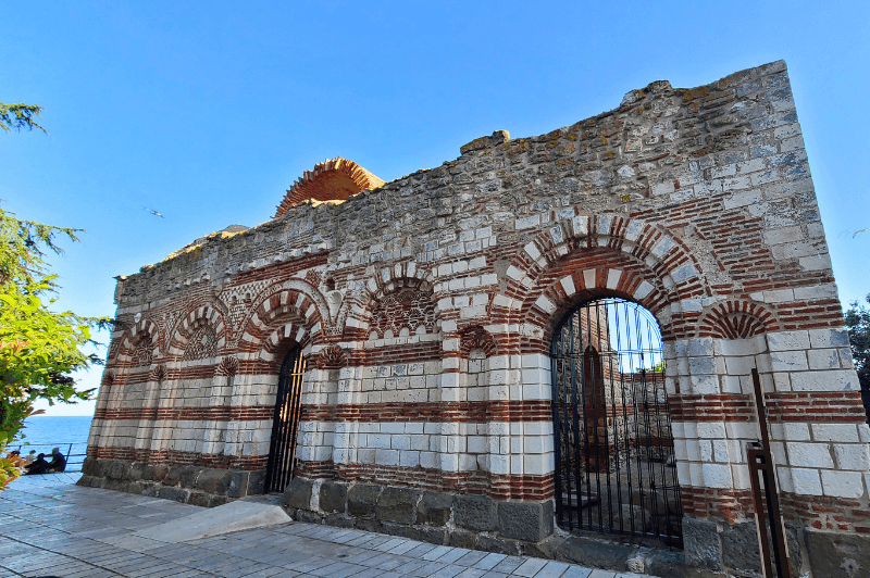 Wide angle shot of the white and red layered ancient brick of St John Alitourgetos Church at the edge of Nessebar, overlooking the sea.