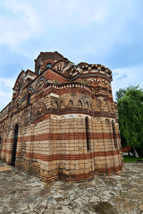 The multi-naved exterior of Christ the Pantocrator Church in Nessebar Bulgaria features stripes of red brick layered amongst white stone.