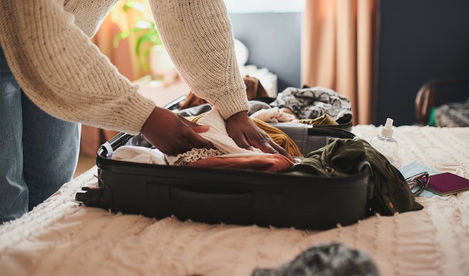 International Travel Packing List Carry-On Bag Restrictions: person packing their things into a carry-on suitcase