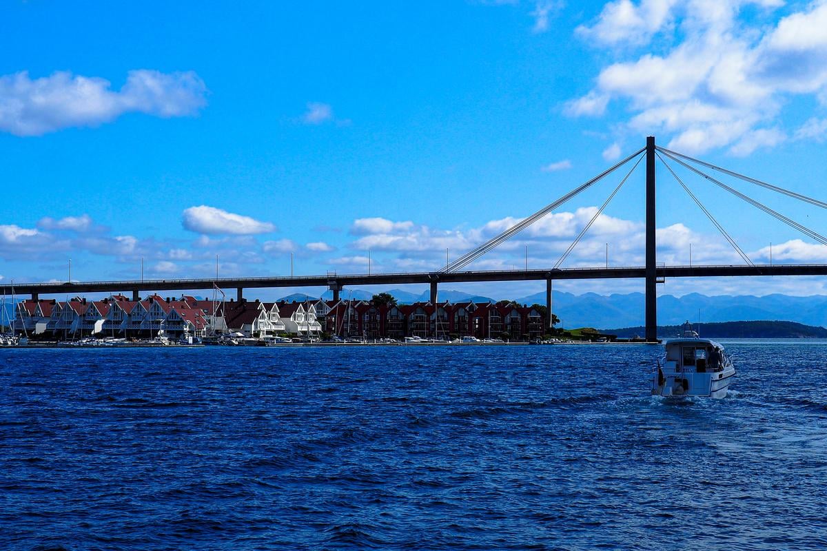 Boat navigating Stavanger harbor with bridge and coastal houses in background, Stavanger, Norway