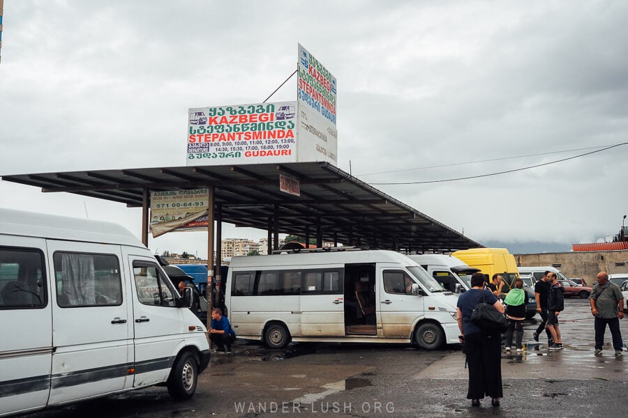 White minivans parked at Didube Terminal in Tbilisi, with passengers waiting around the carpark.