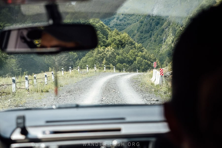 Looking out from a car windscreen at a gravel road with metal safety barricades.