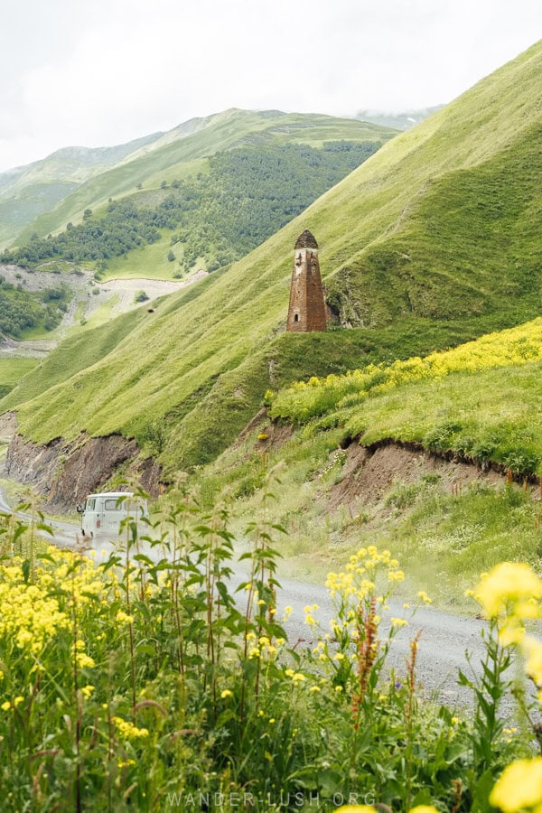 Lebaiskari Tower, a Vaink style defensive tower on a green rise above the road to Shatili, with a grey buhanka van jetting past.