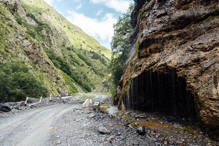 A gaping cave and waterfall on the side of a gravel road in the Caucasus mountains of Georgia.