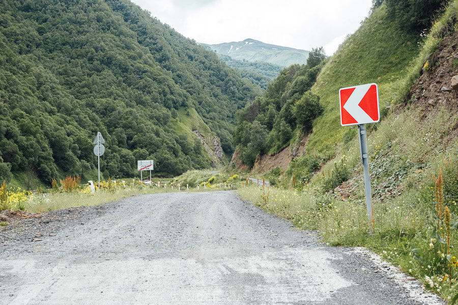 A wide gravel road in Kistani, Khevsureti with red and white road signs.