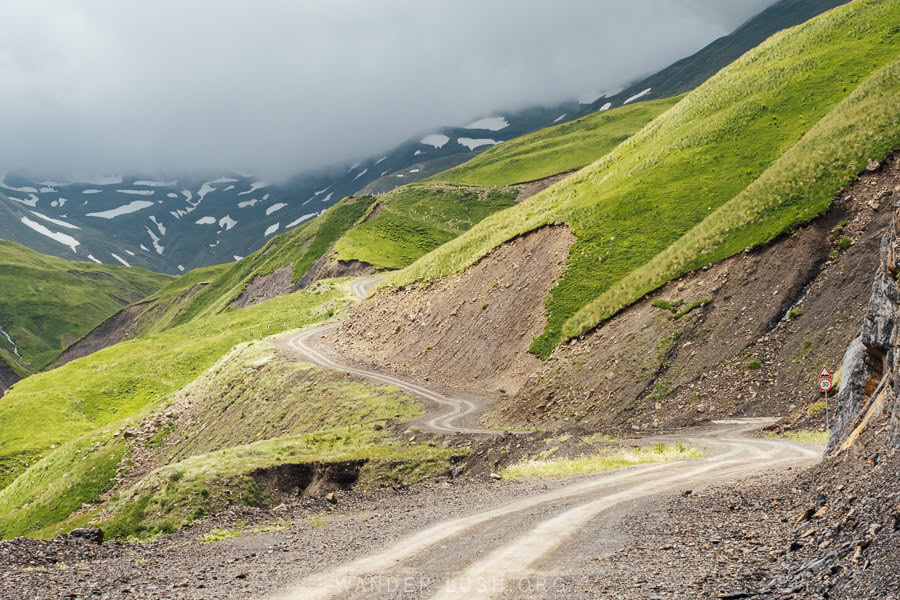 A beautiful gravel road leads towards the Datvisjvari Pass and the high mountains of Khevsureti, with storm clouds gathering at the highest point.