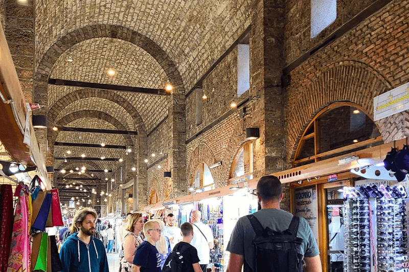 Inside the beautiful arched hallway of the Old Bazaar in central Sarajevo Bosnia. String lights hang from the brick ceiling and the stalls of vendors line the hall.