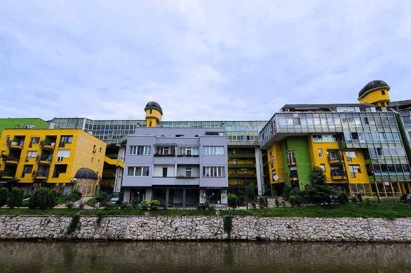 A large blocks long odd soviet style building in Sarajevo painted in bright yellow and green with lots of windows.