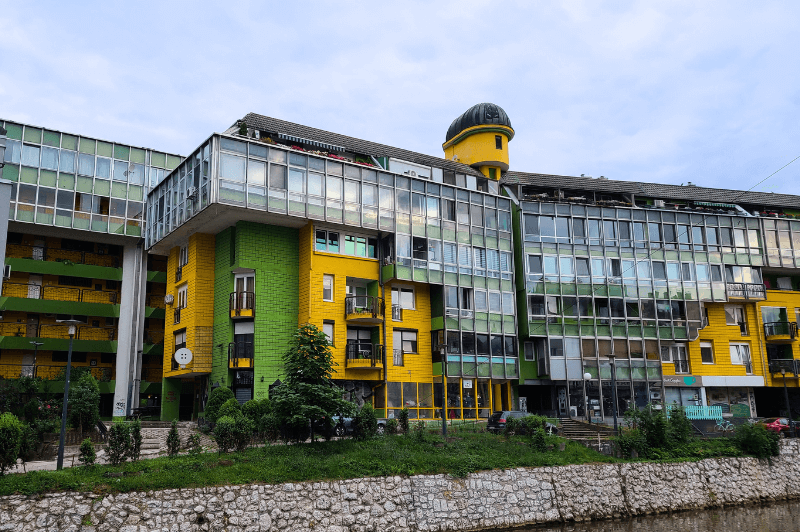 An odd soviet style building in Sarajevo painted in bright yellow and green with lots of windows.