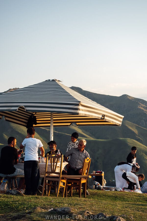 Families sit at a table under an umbrella and enjoy a supra in Bakhmaro, Georgia.