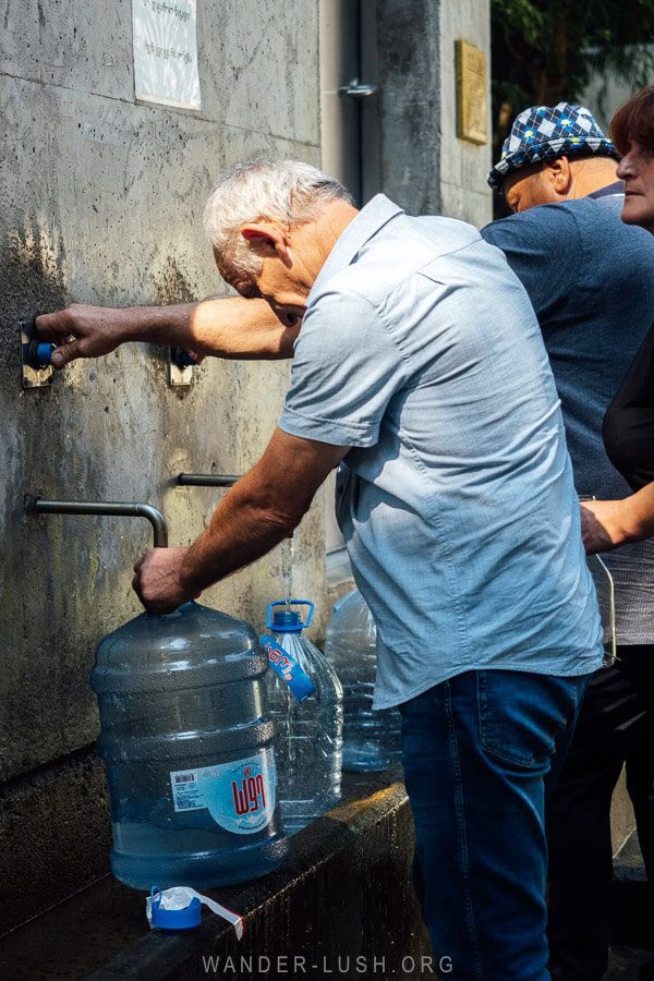 A man fills a large plastic bottle with fresh Nabeghlavi mineral water at a spring in Guria, Georgia.