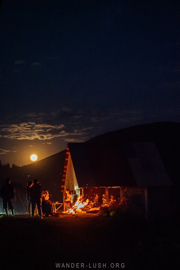 A bonfire in front of a cabin with a full moon in the background in the village of Bakhmaro, Georgia.