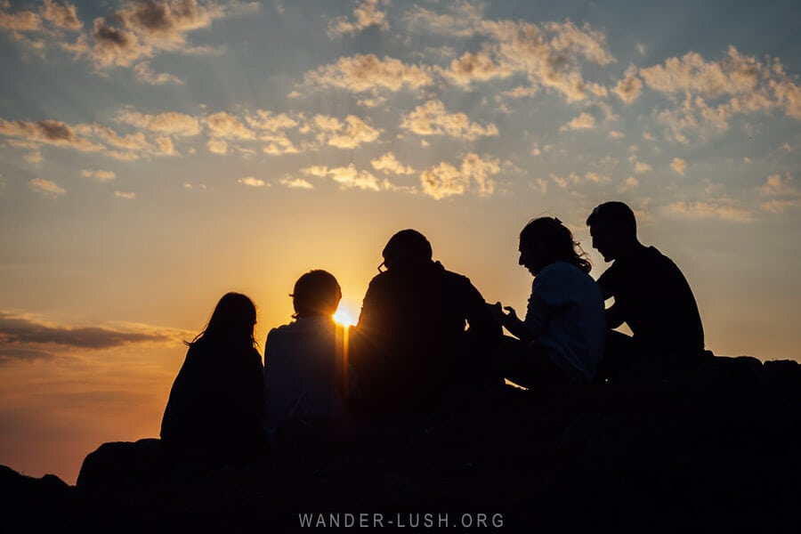 Five friends silhouetted against the sun at a sunset viewpoint in Bakhmaro, Georgia.