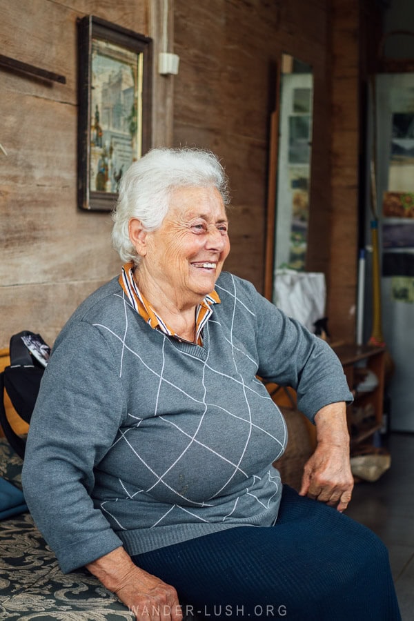 Meri, a woman smiling whilst sitting on a bed on the veranda of a house in Guria.