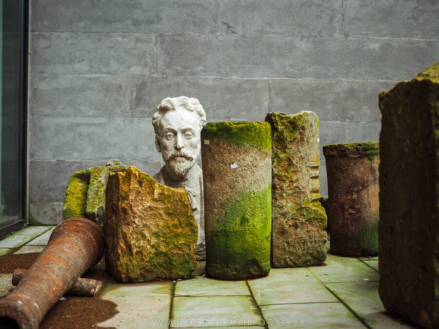 The head of a white stone statue peeks out from behind mouldy stone blocks.