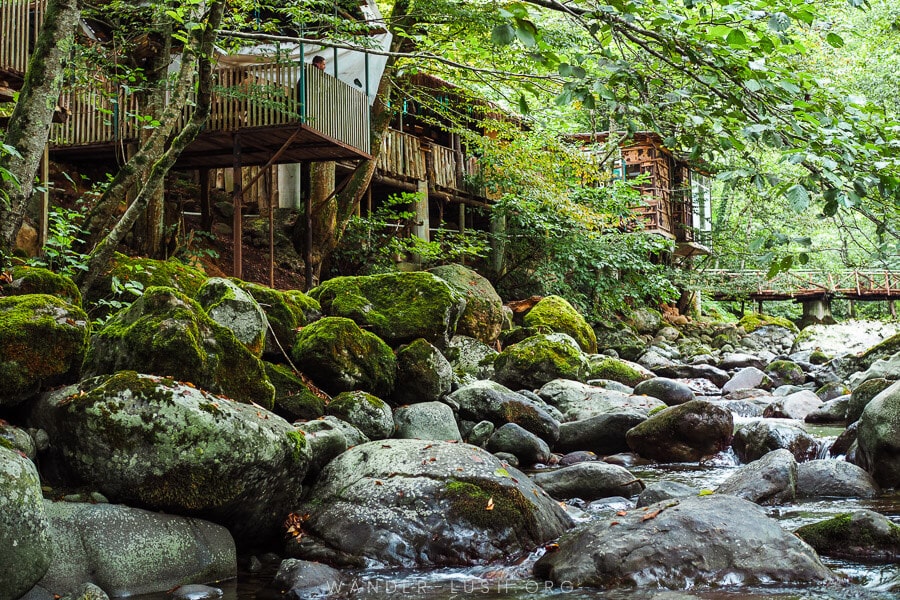 Wooden bungalows over a rocky river bed in Achi, Guria region.