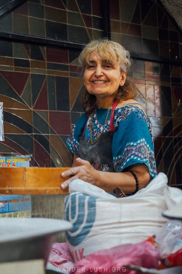 A woman smiles for the camera whilst standing behind her cornflour shop at the Dezerter market in Tbilisi.