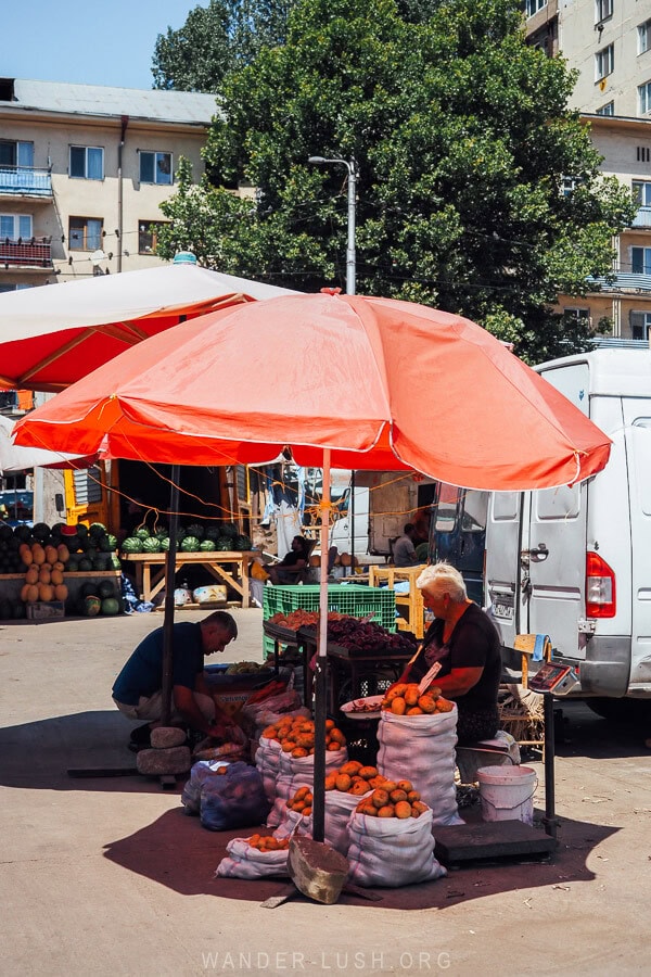 A woman with bags of fruit sits under an umbrella at the Dezerter Bazaar in Tbilisi.