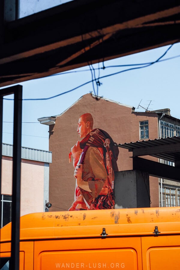 A street mural showing a man carrying a traditional costume on the side of a building near the Dezerter Bazaar.