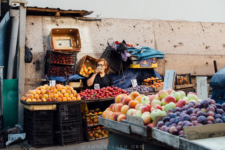 A female vendor sits at a table in front of piles of fruit.