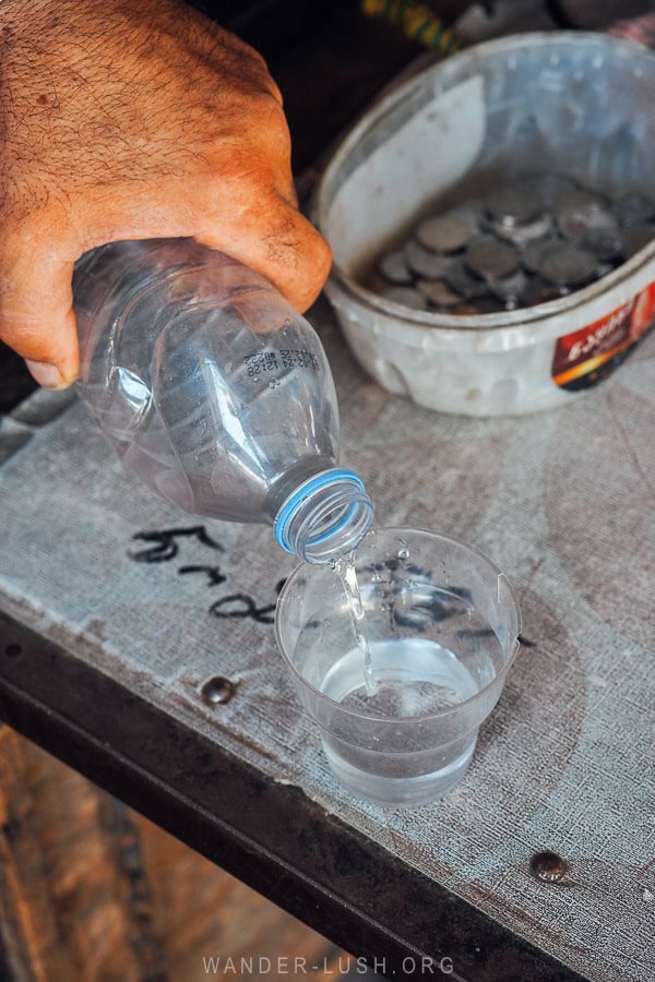 A man pours chacha into a small plastic cup.