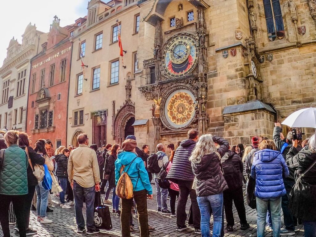 Tourists admiring Prague Astronomical Clock in Old Town Square surrounded by Gothic buildings.