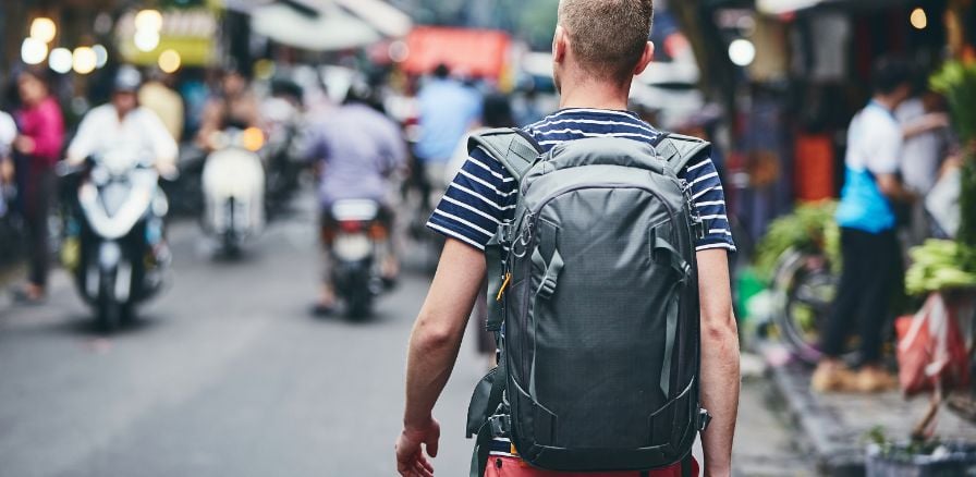 backpacker walking through a busy street, mopeds and street vendors surround traveller