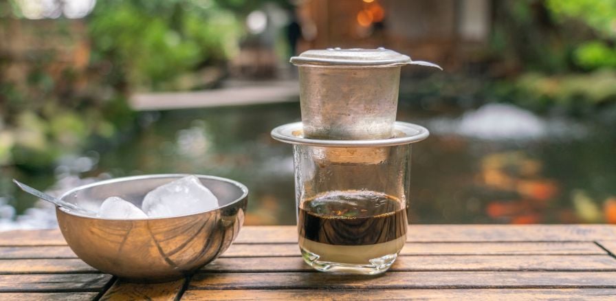 Vietnam coffee, traditional coffee on outdoor table with greenery in background of image 