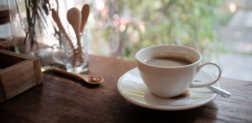 coffee in cup on a saucer on a table in front of a large window looking outside