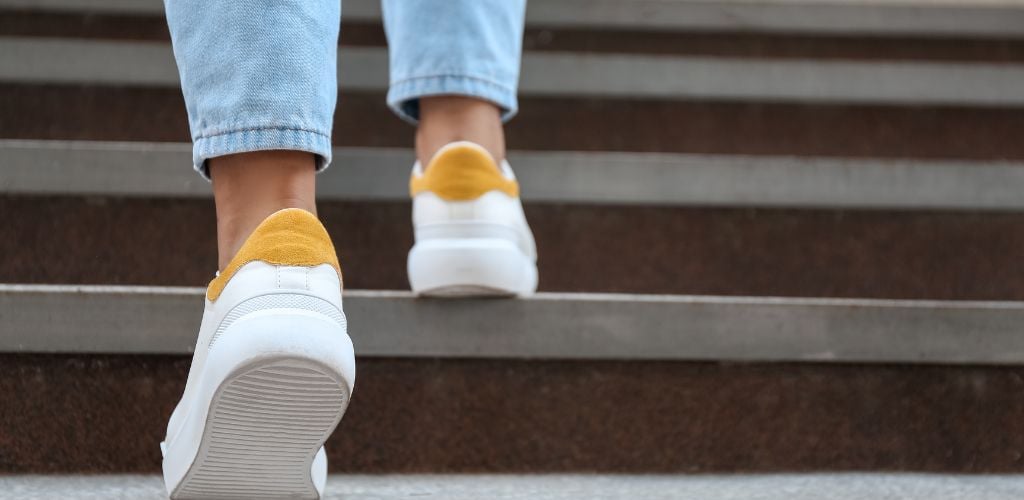 walking city, person walking up the stairs with white and yellow sneakers on and jean pants 