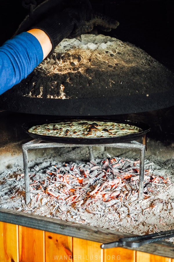 A woman cooks lakror pie under a sac metal lid at a restaurant in Korca, Albania.