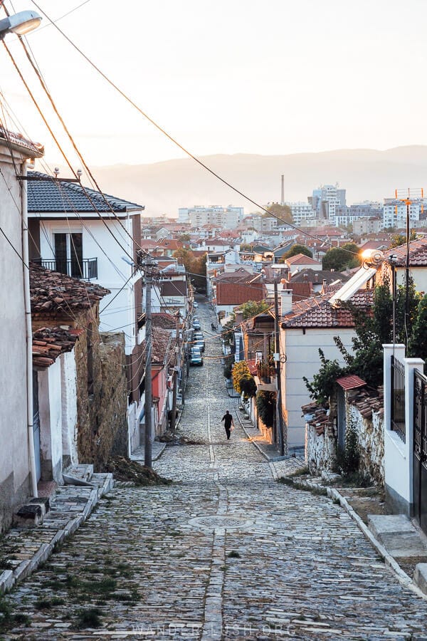 A man walks down a cobbled street in the city of Korca at sunset.