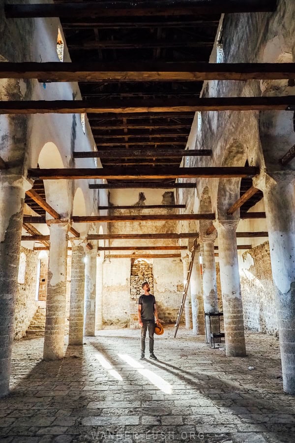 A man stands inside an empty church in Voskopoja with beautiful beams of light streaming through the windows.