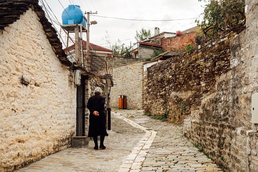 A woman dressed in black walks up an old cobbled street in Permet, Albania.