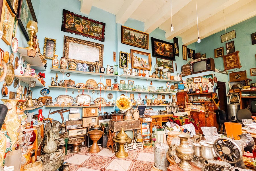 A beautiful antique shop with turquoise painted walls and tall shelves sporting vintage and second-hand goods.