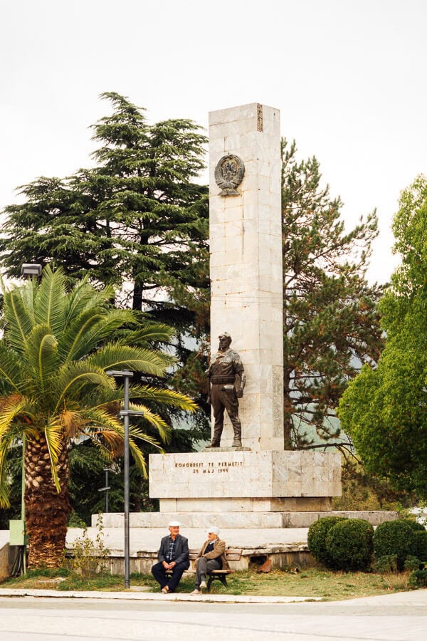 The Permet Congress Statue, a tall concrete monument with two men sitting on a bench below.