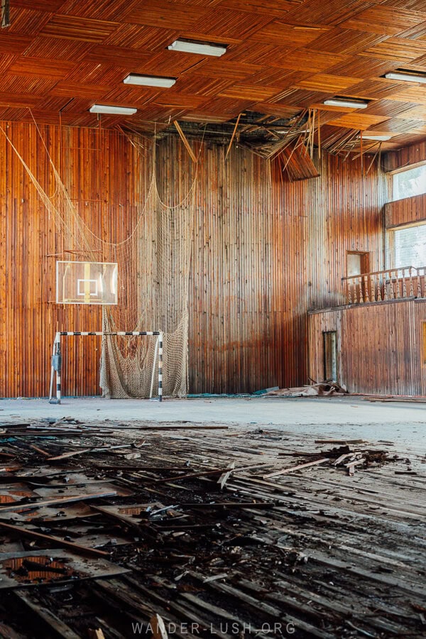 An abandoned indoor basketball court with wood peeling off the floor.