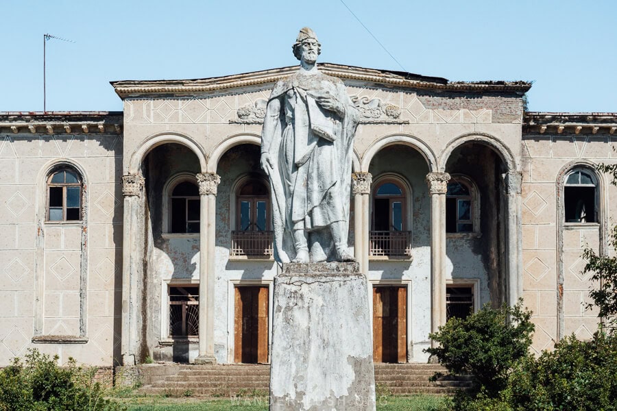 A statue of Shota Rustaveli standing in front of the abandoned culture house in Kakhati, Samegrelo.