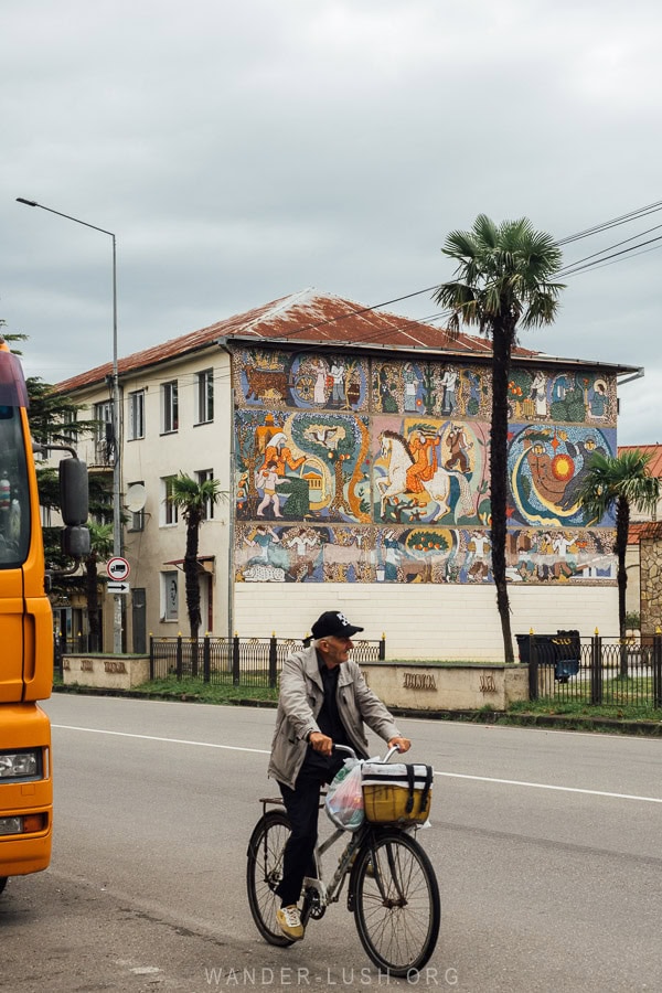 A man rides a bicycle past a Soviet mosaic in Abasha, Georgia.